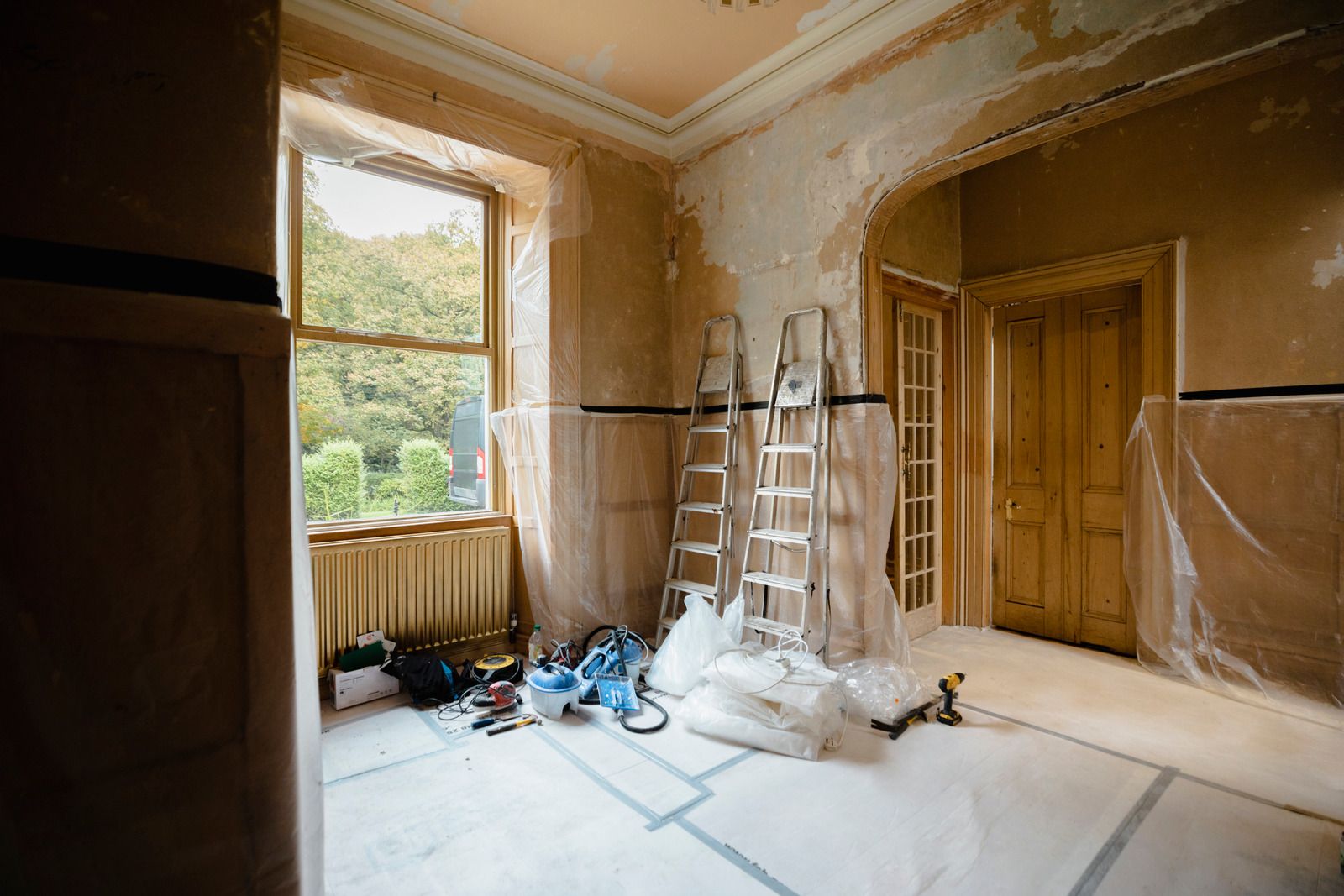 Rum i et ældre hus under renovering med stiger, afdækning, værktøj og dagslys gennem vinduet