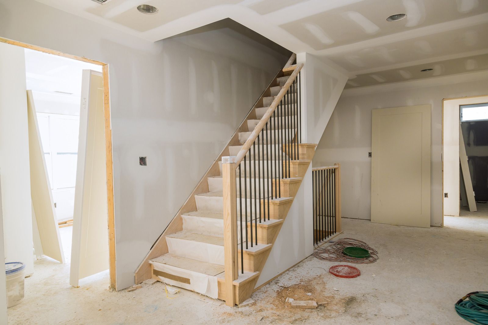 Ny trætrappe og spartlede gipsvægge i et hus under totalrenovering med byggestøv på gulvet